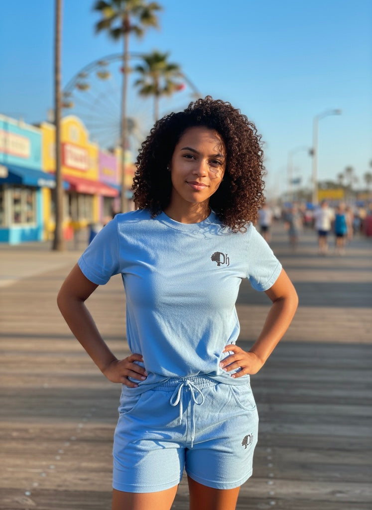 Woman wearing a light blue t-shirt and shorts with a logo on a boardwalk.