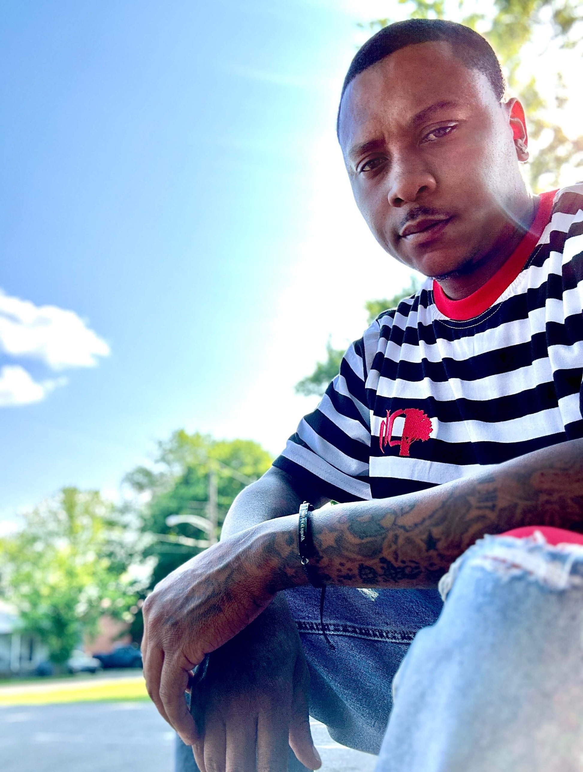 A person wearing a striped cotton t-shirt in a classic fit with a logo on the chest, sitting outdoors.#color_black-stripes