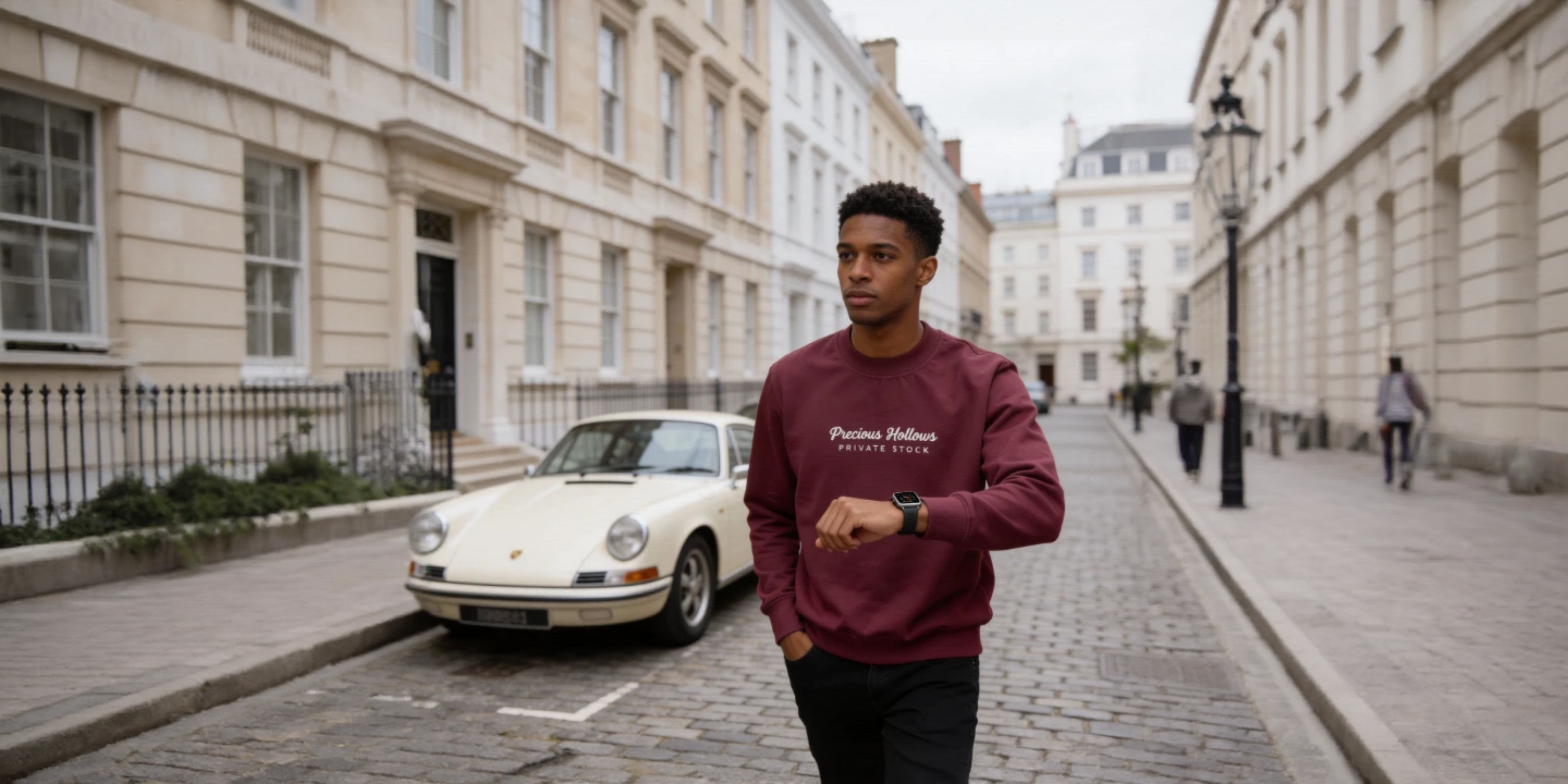 Person wearing a maroon sweatshirt with text, standing on a street with a white car and buildings in the background.