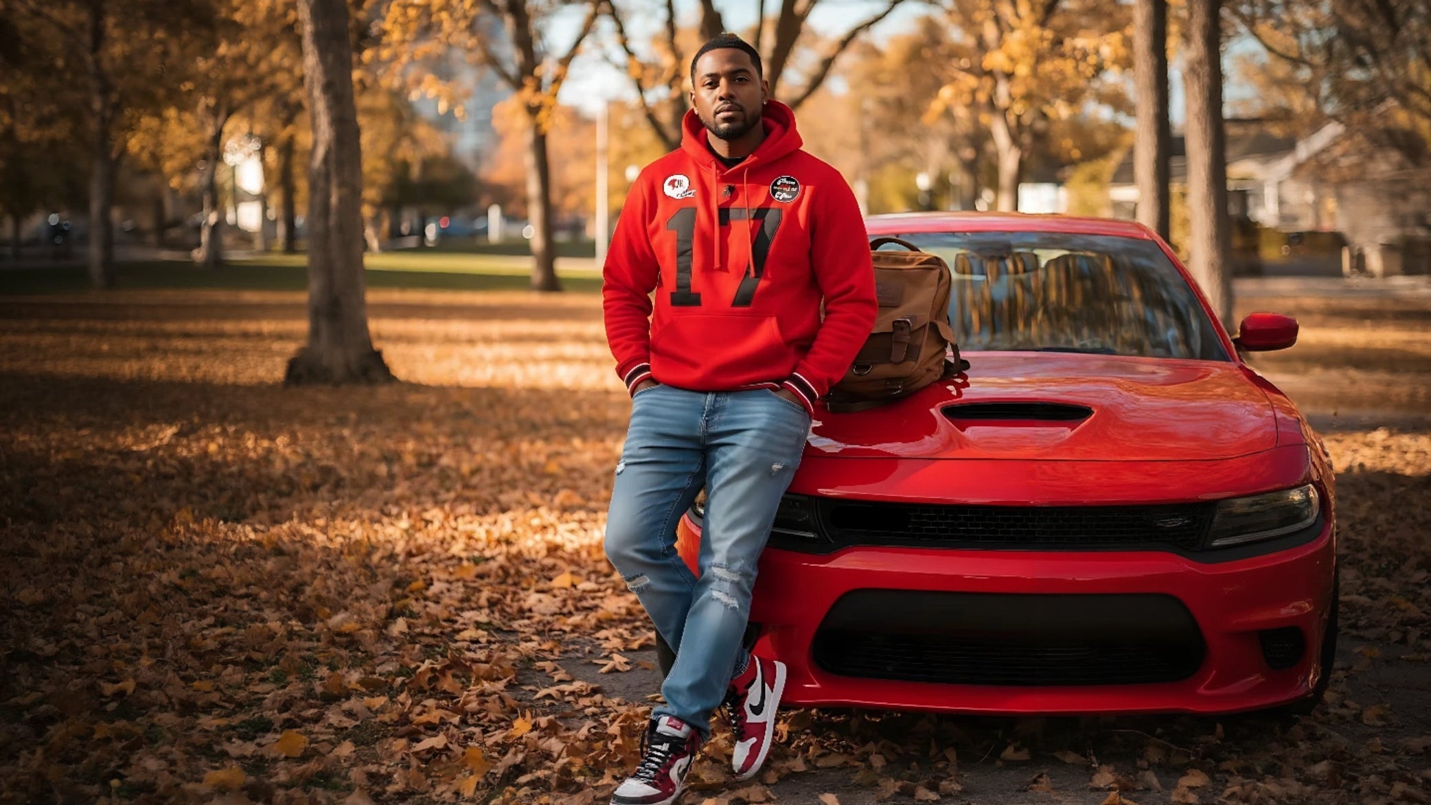 Person in a red hoodie leaning against a red sports car in a park with autumn leaves.