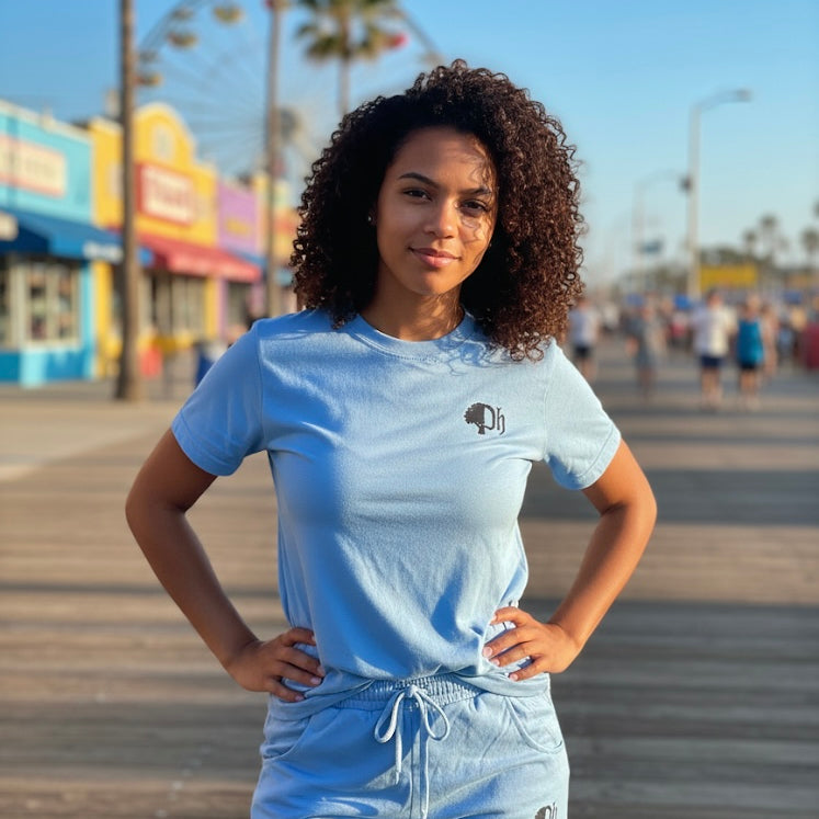 Woman wearing a light blue t-shirt and shorts with a logo on a boardwalk.