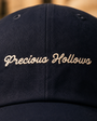 Close view of Precious Hollows script embroidery on the navy cap