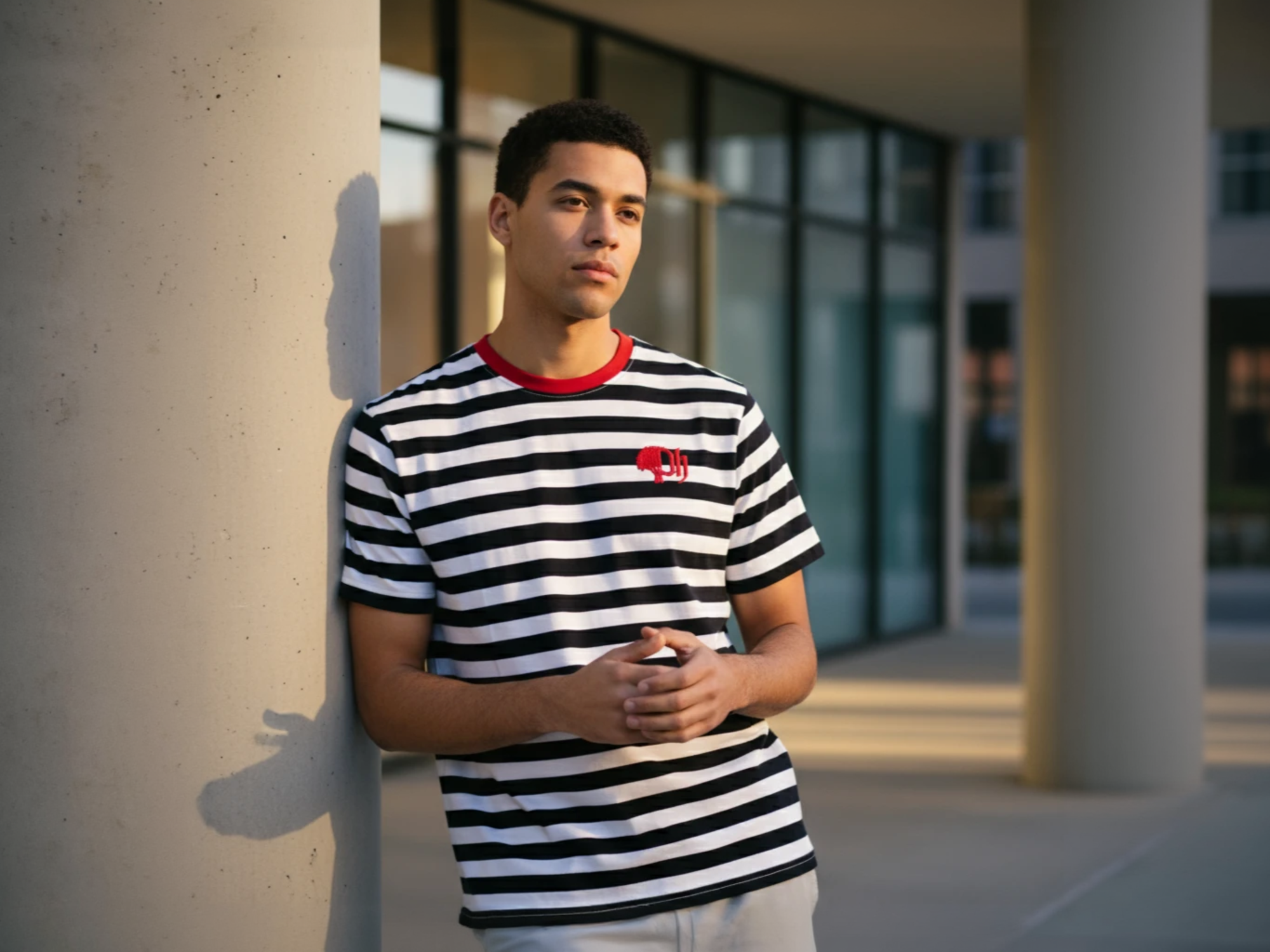 Person wearing a black and white striped shirt with a red collar, standing against a building exterior.