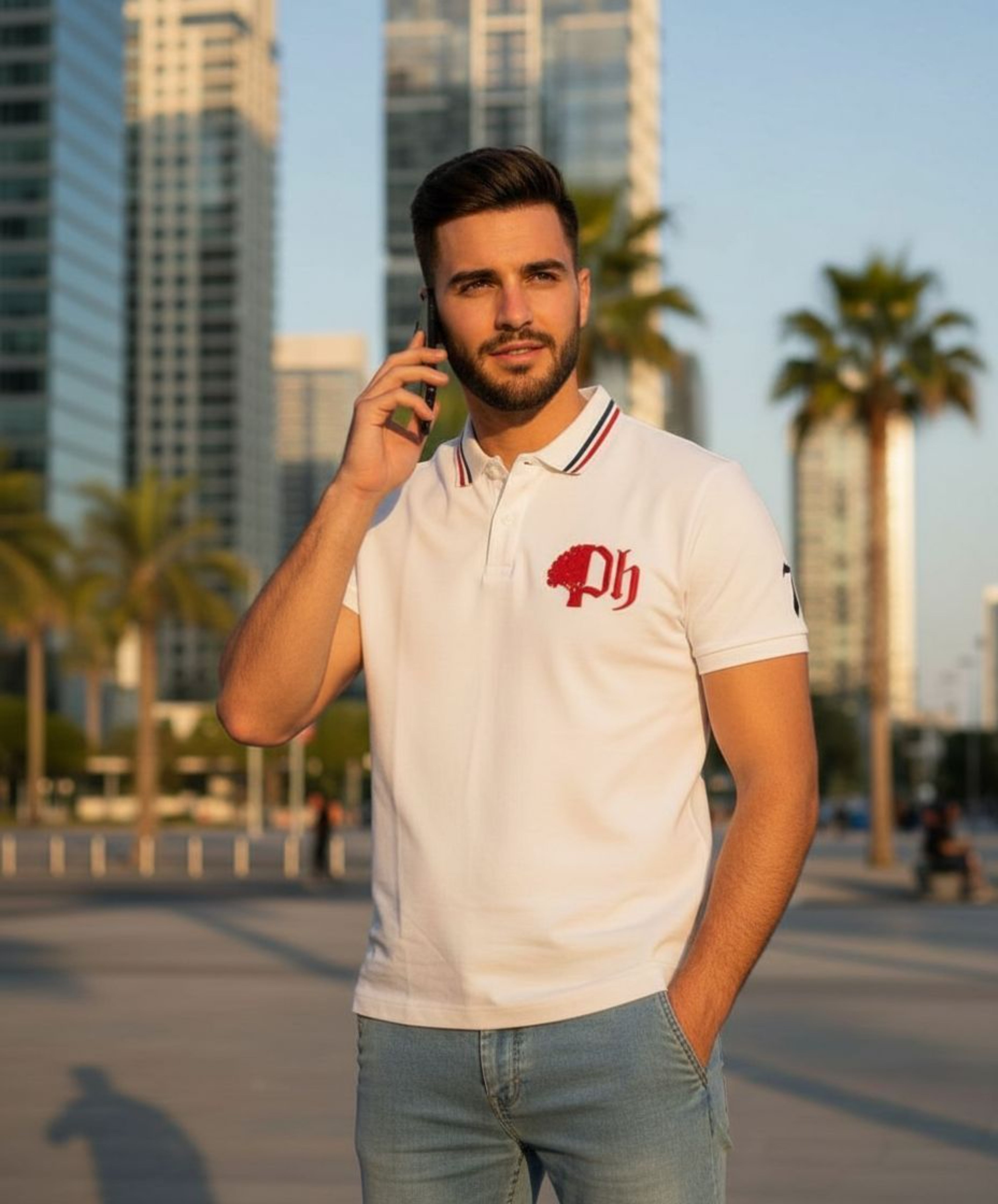 A man standing talking on the phone with a city scape and palm trees in the  background