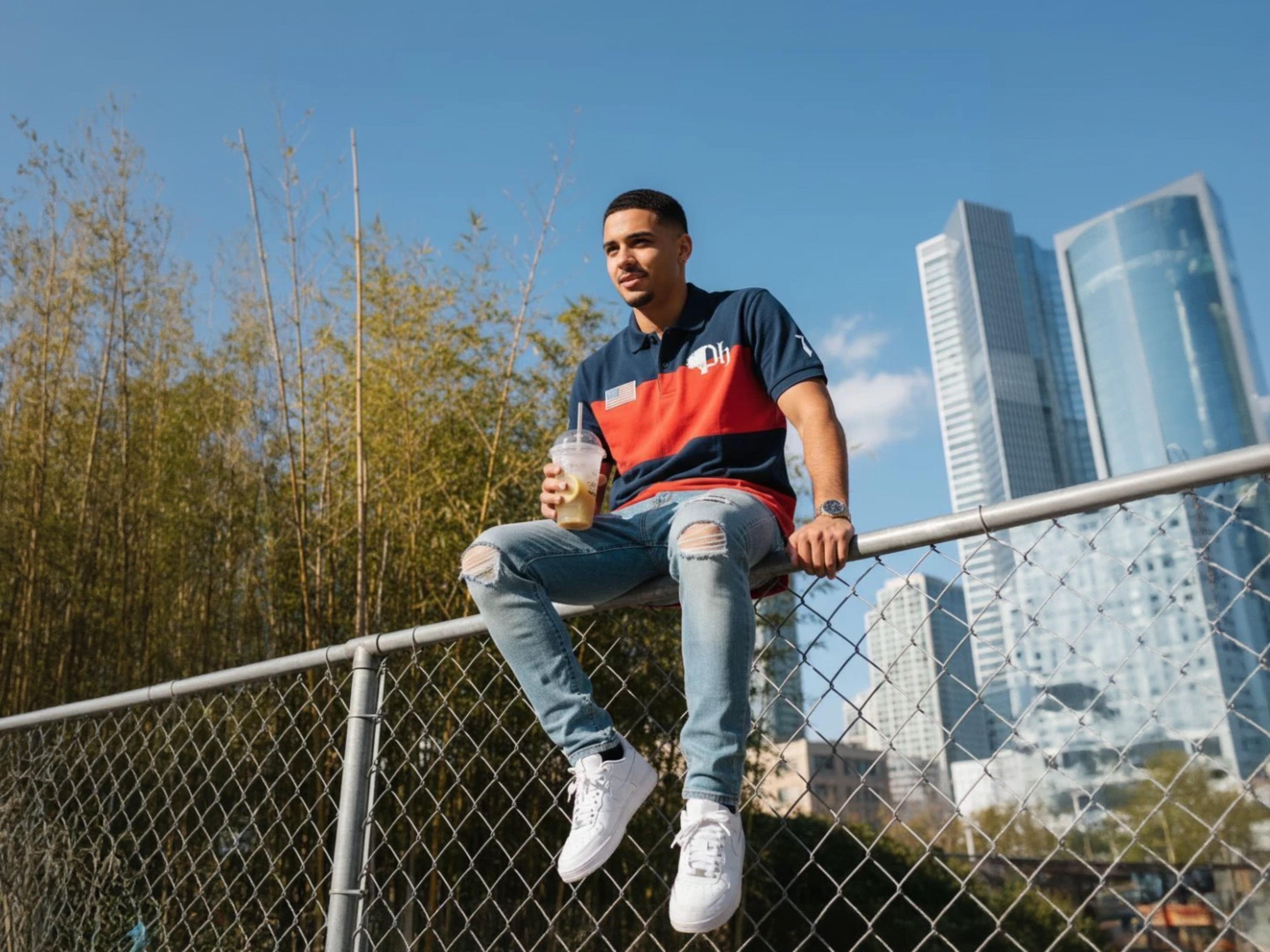 A man sitting on a fence with a city scape behind him in the background