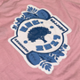 Blue and white logo on a pink shirt.#color_pink