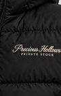 Close-up of a black puffer jacket with Off White embroidered text reading 'Precious Hollows PRIVATE STOCK' on the chest.