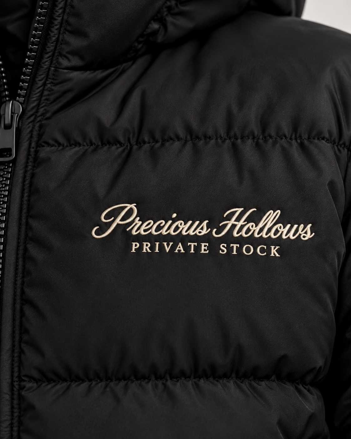 Close-up of a black puffer jacket with Off White embroidered text reading 'Precious Hollows PRIVATE STOCK' on the chest.